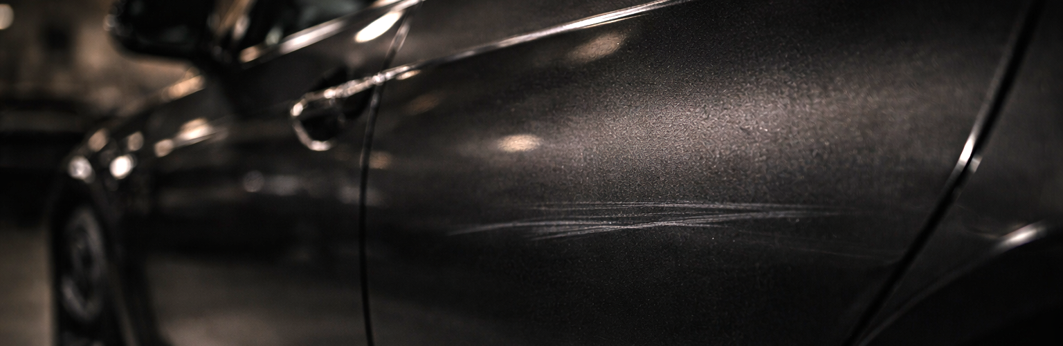 Close-up van een donkere auto met een kras op het portier (werkplaats)